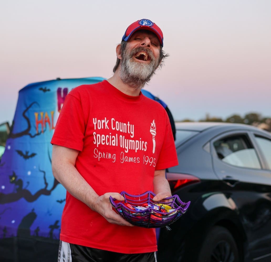 A TLC individual in a red shirt hold a basket of candy during a Halloween event.