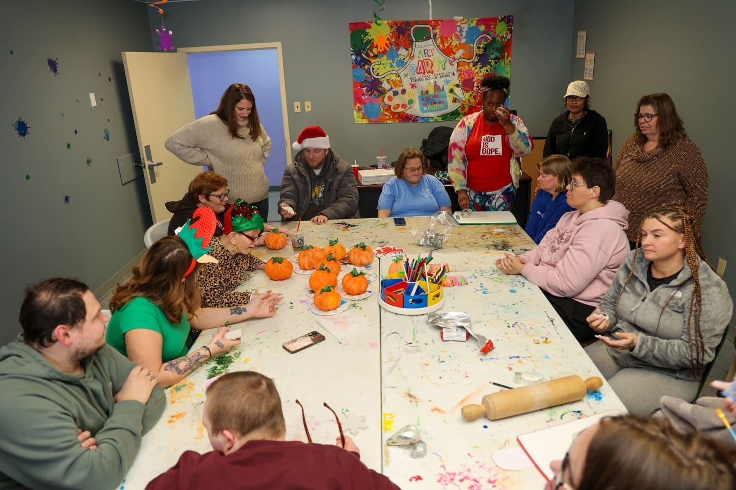 TLC day program participants and staff gather around a table covered in art supplies and painted pumpkins during a creative group activity.
