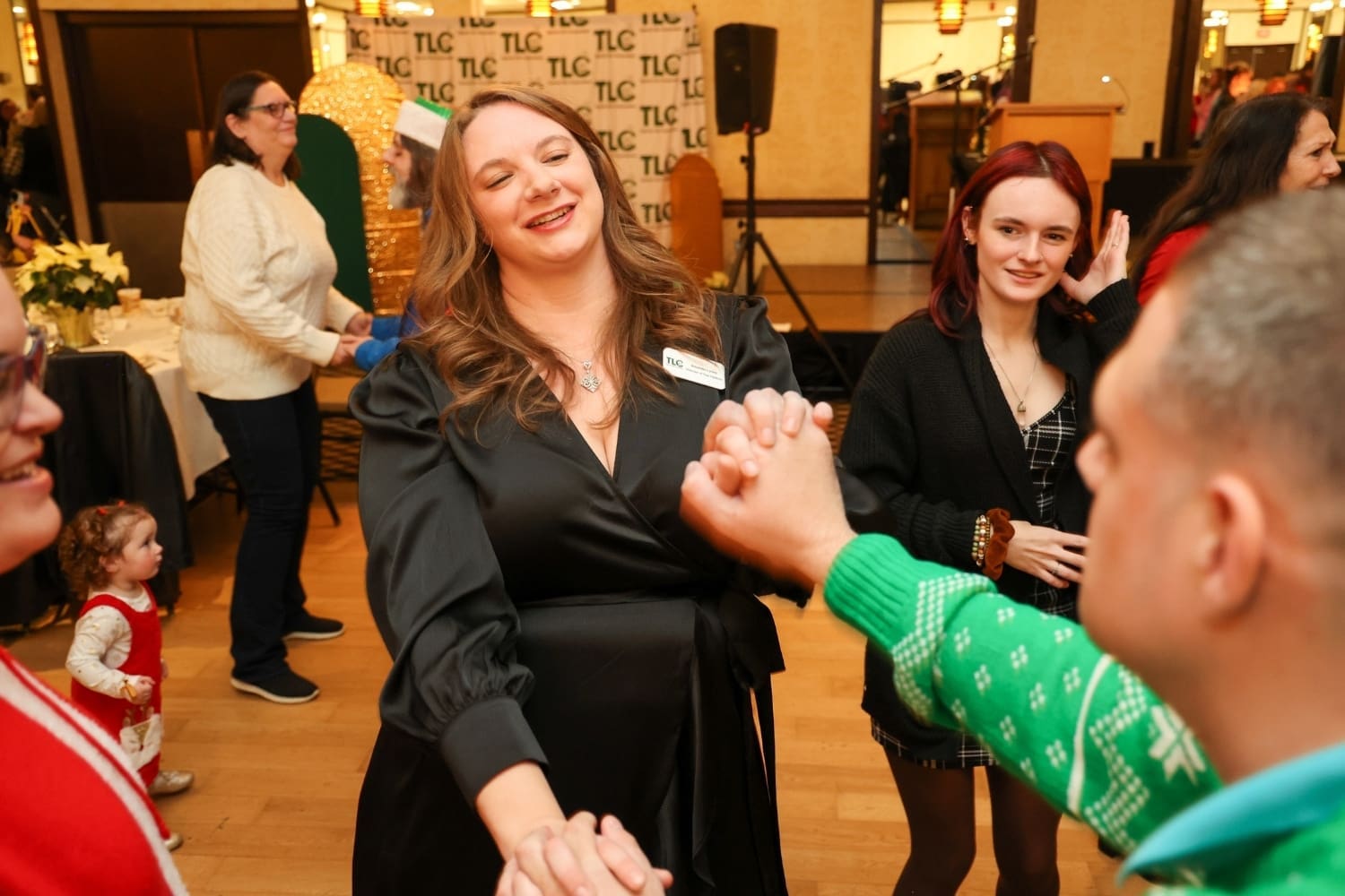 A TLC staff member smiles while dancing and holding hands with program participants during a community event.