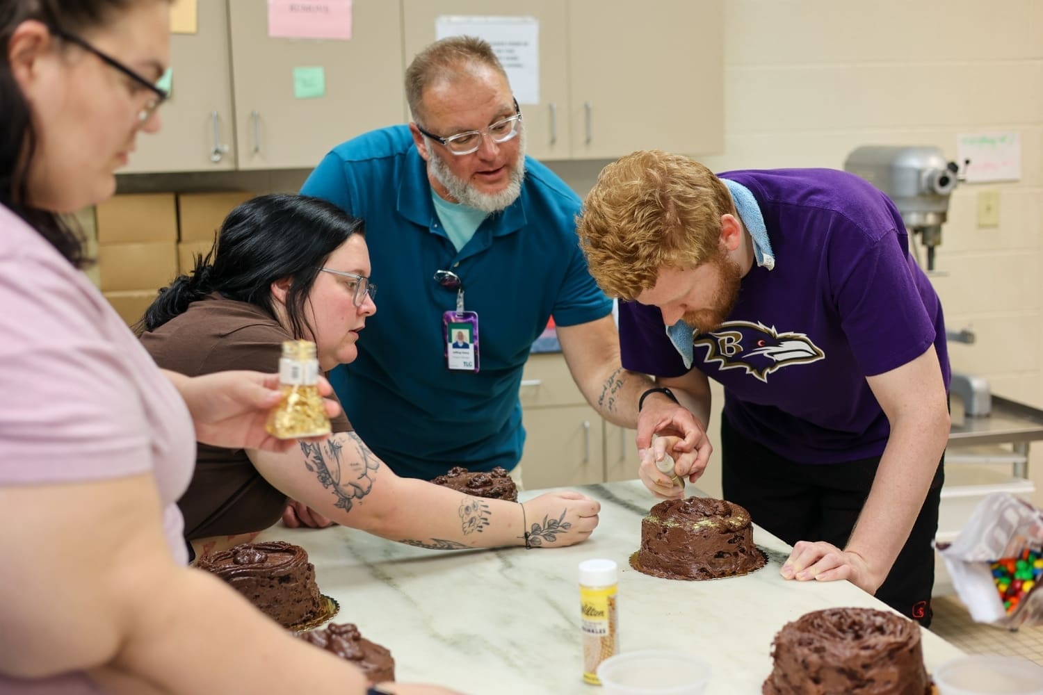 TLC staff and program participants work together in a kitchen to decorate chocolate cakes during a baking activity.